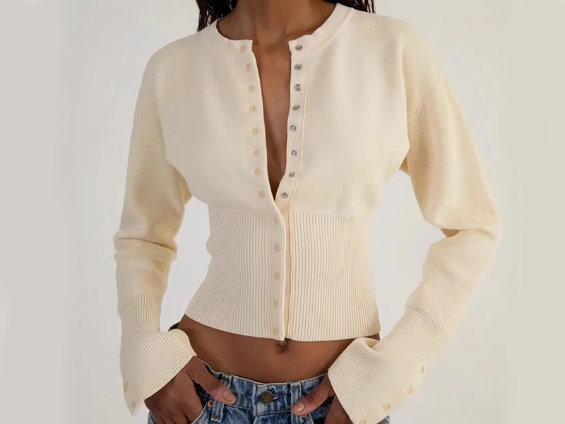 Women's cream knit cardigan with button-front closure, ribbed waist detail, and long sleeves, styled with denim jeans for a modern casual look.