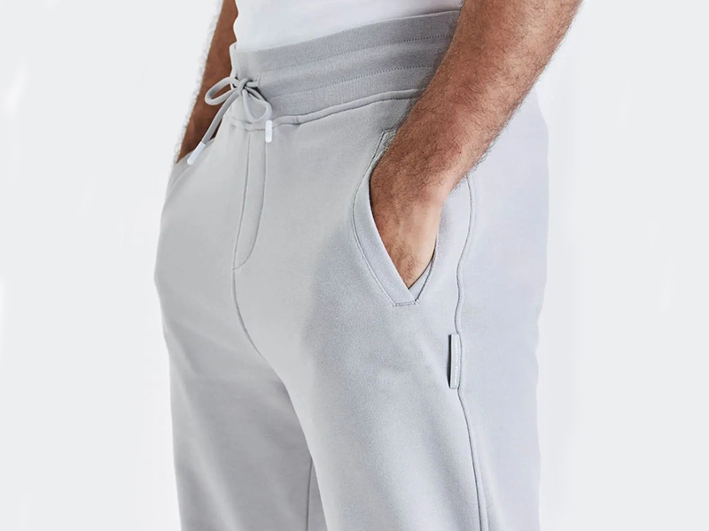 Close-up of light gray men's jogger sweatpants with drawstring waist, side pockets, and soft fleece fabric for casual comfort.