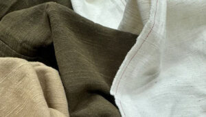 Close-up of slub fabric in natural beige, brown, and white tones, showcasing irregular woven texture, visible yarn variations, and organic textile characteristics.