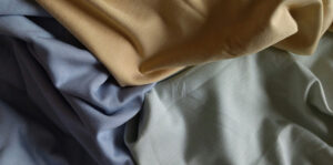 Close-up of three folded sportswear fabrics in beige, blue, and gray, showing texture and stretch."
