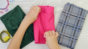 Hands stretching colorful fabric samples beside measuring tape and sewing accessories for leggings material selection and textile quality evaluation