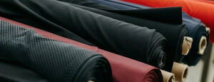 Rolls of various stretch fabrics in black, red, and navy, neatly arranged on cardboard tubes in a fabric warehouse.