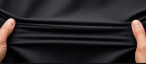 Hands stretching black spandex fabric to demonstrate exceptional elasticity, smooth texture, and flexible performance material used in activewear and sportswear.