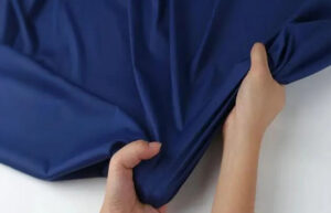Hands pulling and stretching a piece of navy nylon fabric, showing its elasticity and smooth texture suitable for activewear or outdoor apparel.
