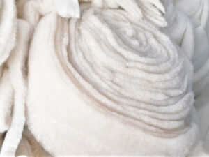 Rolled white synthetic insulation fabric with soft lofted texture, designed for warmth, lightweight comfort, and moisture-resistant performance in outdoor apparel.