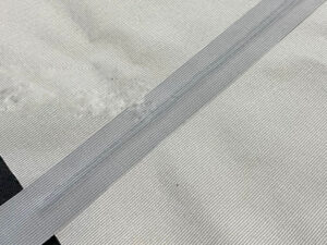 Close-up of white tricot tape applied to fabric seam for reinforcement and durability in garment construction.
