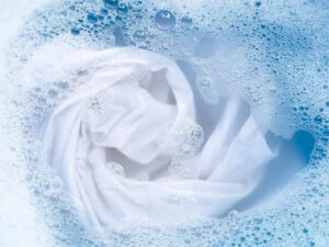 White fabric soaking in soapy water with foam bubbles during gentle laundry washing process.