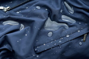 Waterproof performance fabric with water droplets beading on the surface, demonstrating durable water-resistant coating and weatherproof outdoor apparel protection.