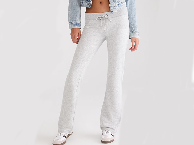 Woman wearing light gray sweatpants with drawstring and white sneakers, standing against plain background.