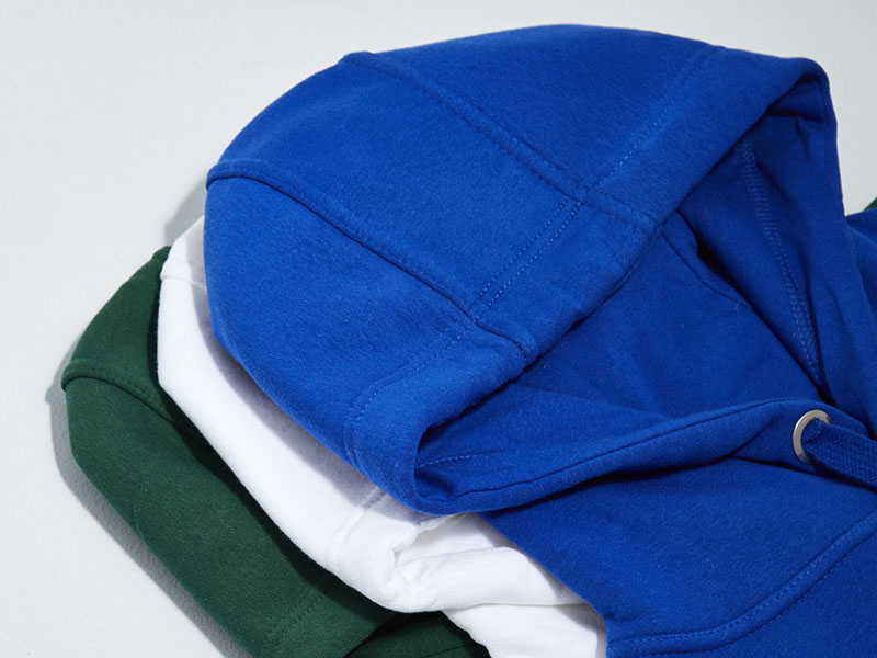 Folded heavyweight hoodies in blue, white, and green colors, showcasing thick cotton fabric, durable construction, and premium casual streetwear style.