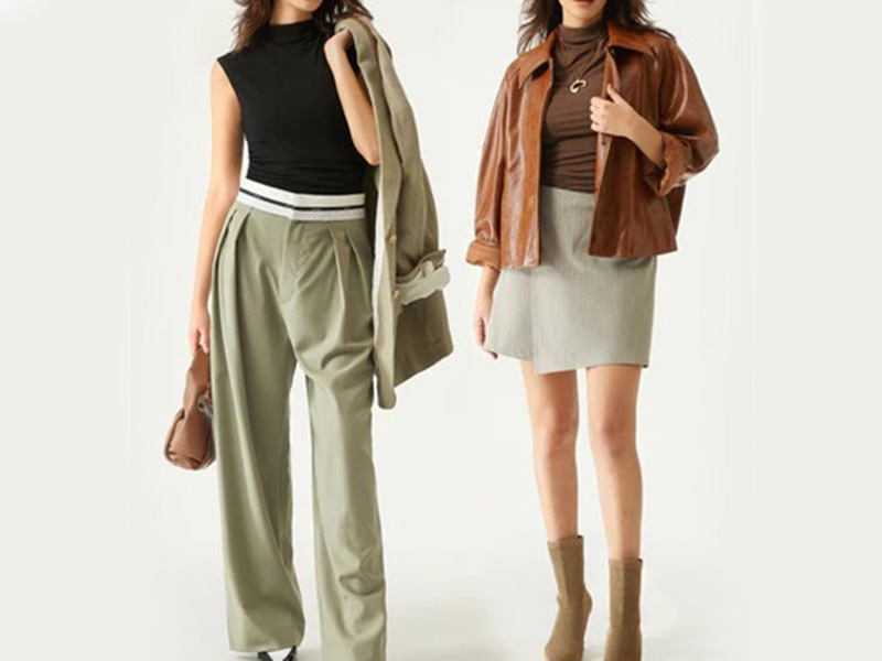 Two women wearing fall outfits with one in high-waisted trousers and sleeveless top, the other in a mini skirt with brown leather jacket.