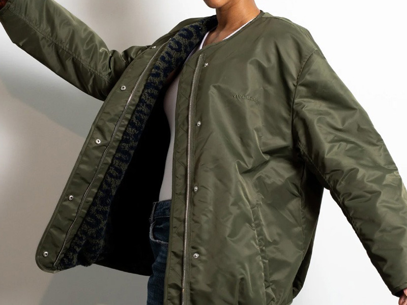 Person wearing an olive green bomber jacket with quilted lining, showcasing insulated nylon fabric, snap-button closure, and casual military-inspired outerwear design.