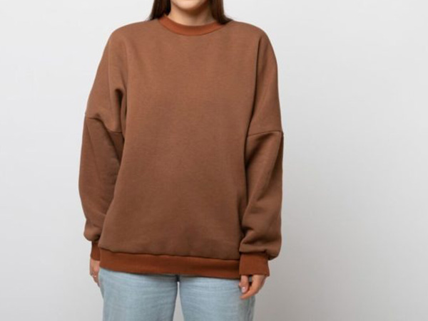 Woman wearing oversized brown crewneck sweatshirt with relaxed fit and casual minimalist streetwear style against plain background