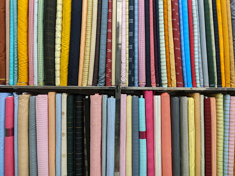 Multiple colorful fabric rolls neatly arranged on shelves in textile store showcasing various materials, patterns, and apparel fabrics.