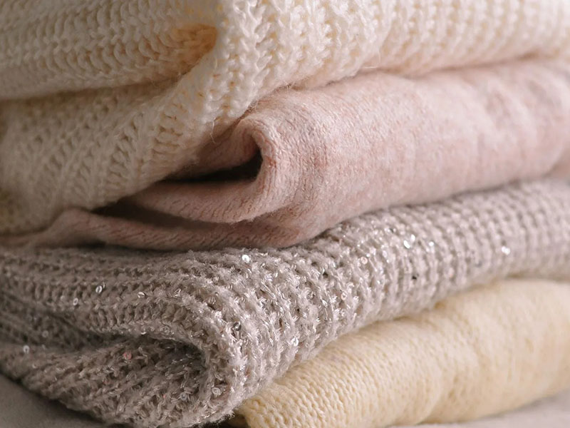 Close-up of stacked soft knit fabrics in cream, pink, and gray textures.