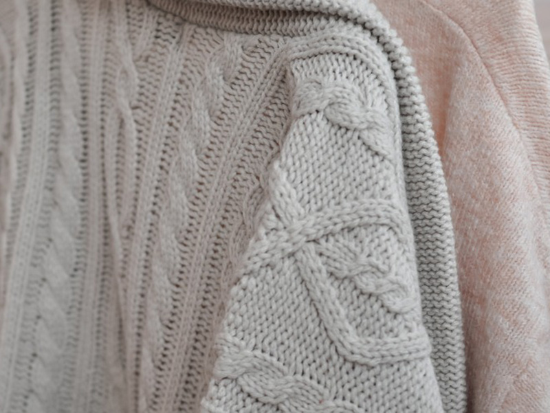 Close-up of beige and pink cable-knit sweaters showing detailed woven patterns.