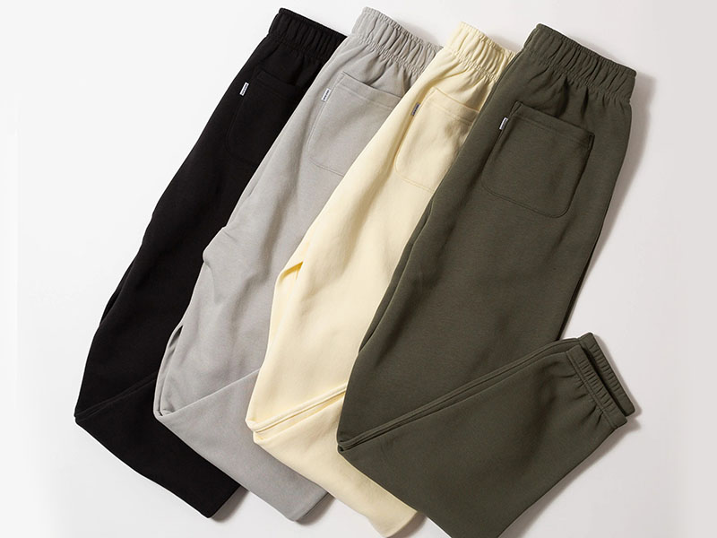 Fleece sweatpants in black, gray, cream, and olive colors, featuring elastic waistbands and tapered legs for comfortable casual wear.