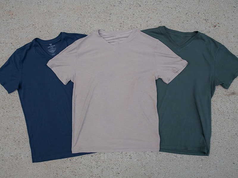 Three casual V-neck long sleeve tops in beige, blue, and olive hanging on hangers in a retail display.