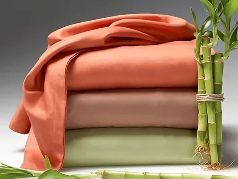 Folded bamboo fabric in earthy tones with bamboo stalks beside.