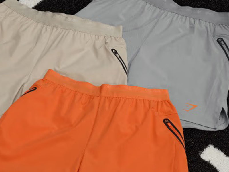 Lightweight running shorts in orange, gray, and beige with elastic waistbands and zippered pockets for athletic training and outdoor activities.