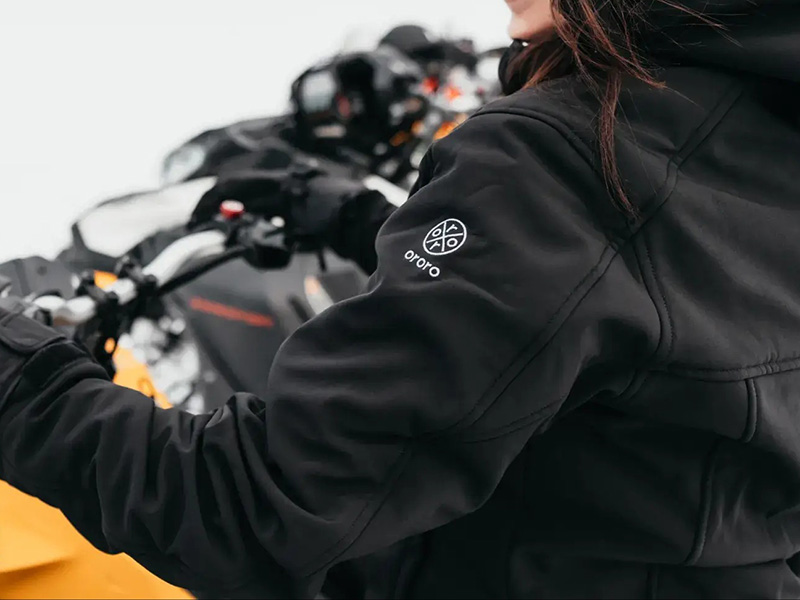 Woman wearing black heated jacket while riding motorcycle outdoors in cold weather