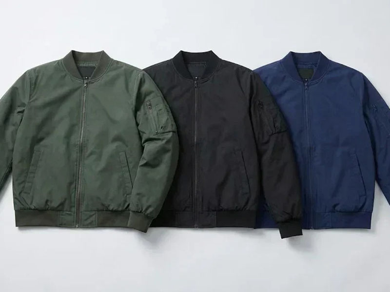 Three bomber jackets in olive green, black, and navy blue displayed side by side, featuring zip-front closures, ribbed cuffs, and military-inspired casual outerwear design.
