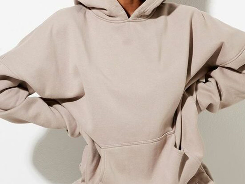 Close-up of person wearing oversized beige mushroom-colored hoodie with relaxed fit and front pocket, arms bent at waist