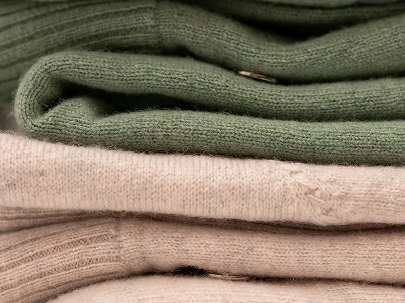 Close-up of neatly folded cashmere sweaters in soft green, cream, and beige colors.