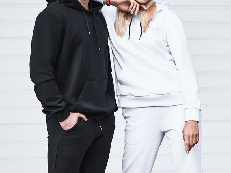 Man and woman wearing matching black and white hooded tracksuits, showcasing comfortable fleece hoodies and joggers for casual everyday wear.