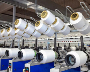 Multiple spools of white yarn arranged on automated spinning machines in textile factory.